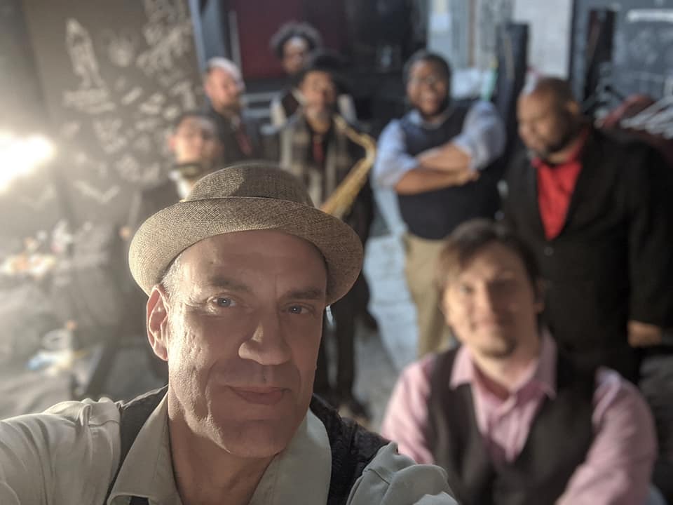 John Jay Myers in a fedora with the full band behind him backstage